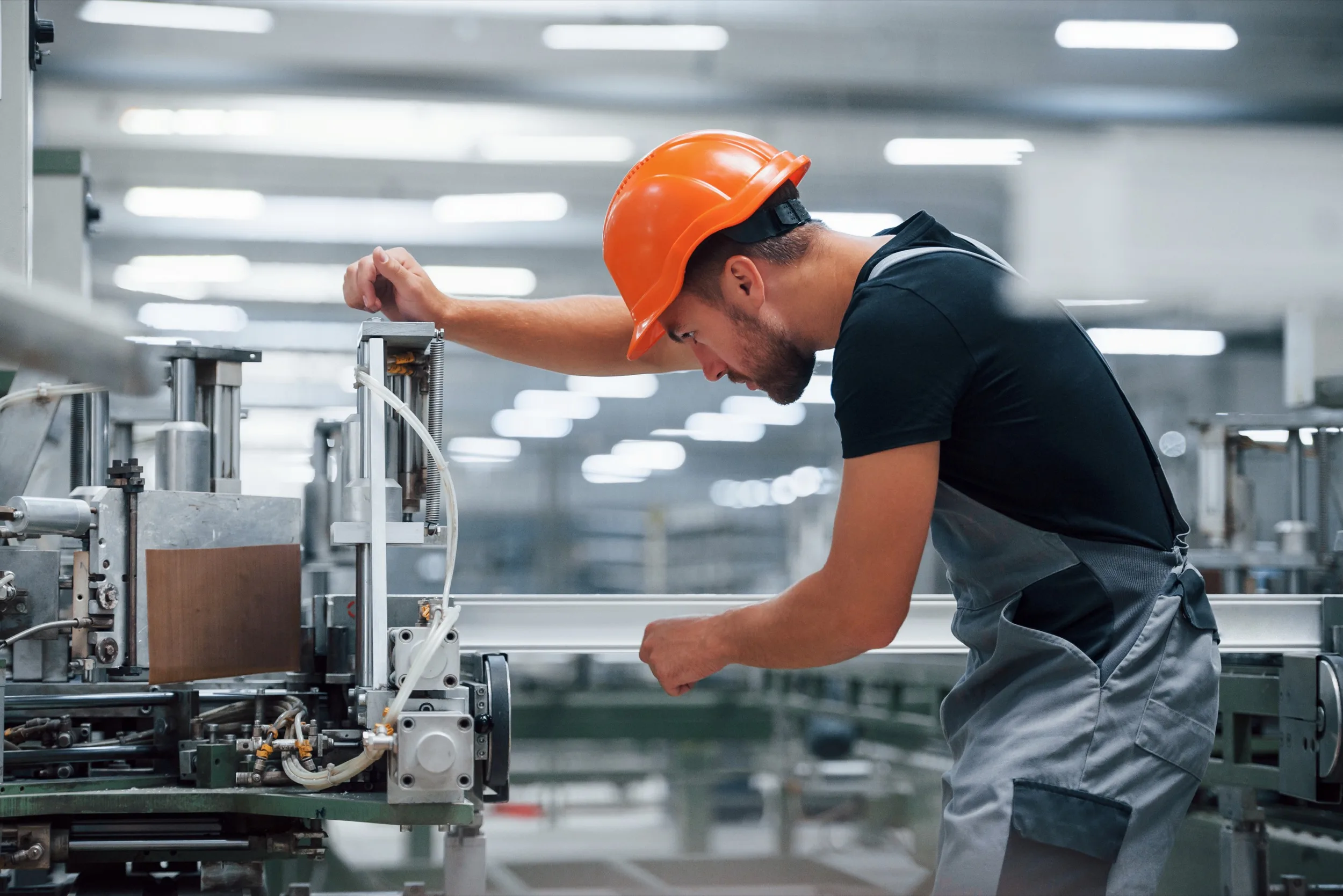 A technician in an orange hard hat working at a machine on a factory floor