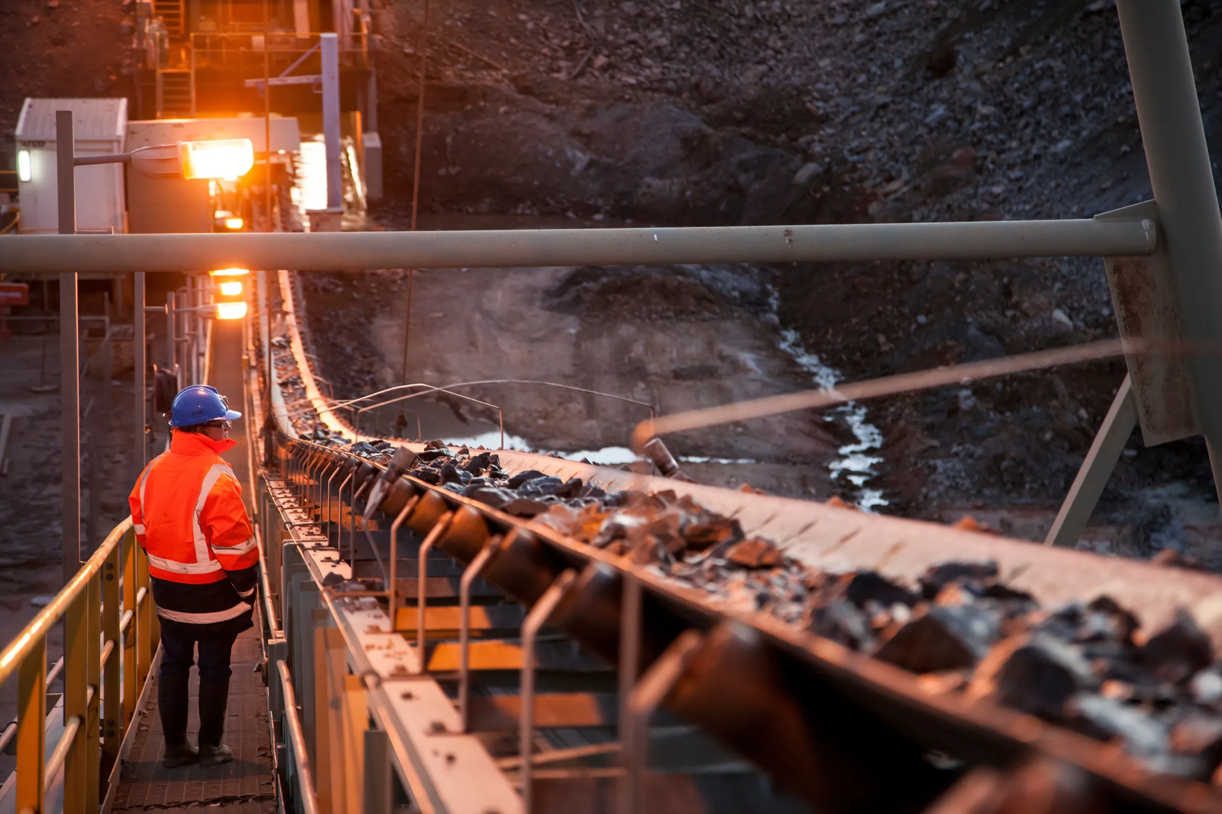 A worker in high-visibility clothing beside a conveyor in an underground mine